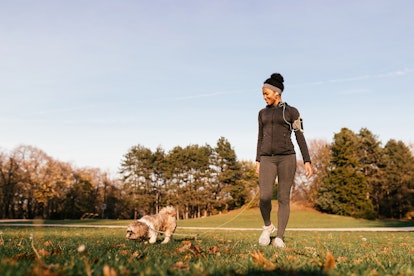 Happy African American athletic woman enjoying while walking her dog in nature. 